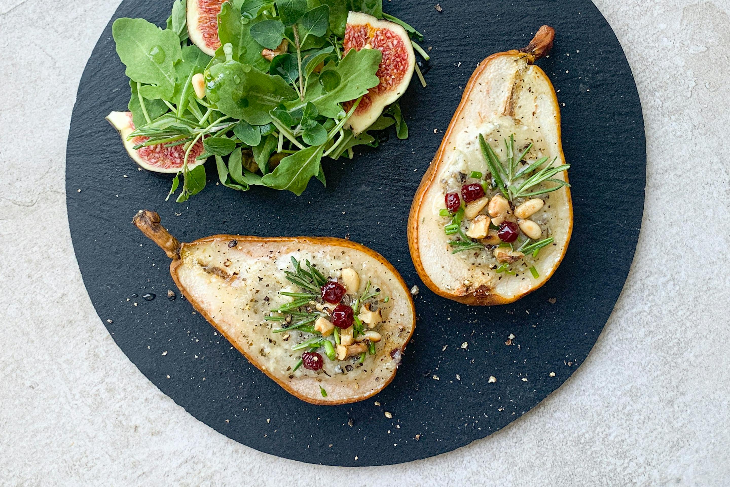 2 gefüllte Birnenhälften auf einem schwarzen Schieferteller mit Beilagensalat und Feigen